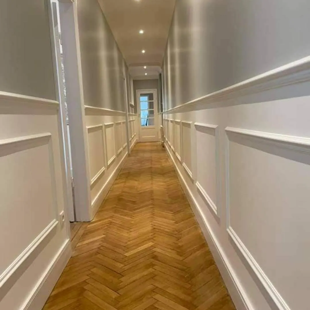 Couloir étroit avec soubassements moulurés blancs et parquet chevrons